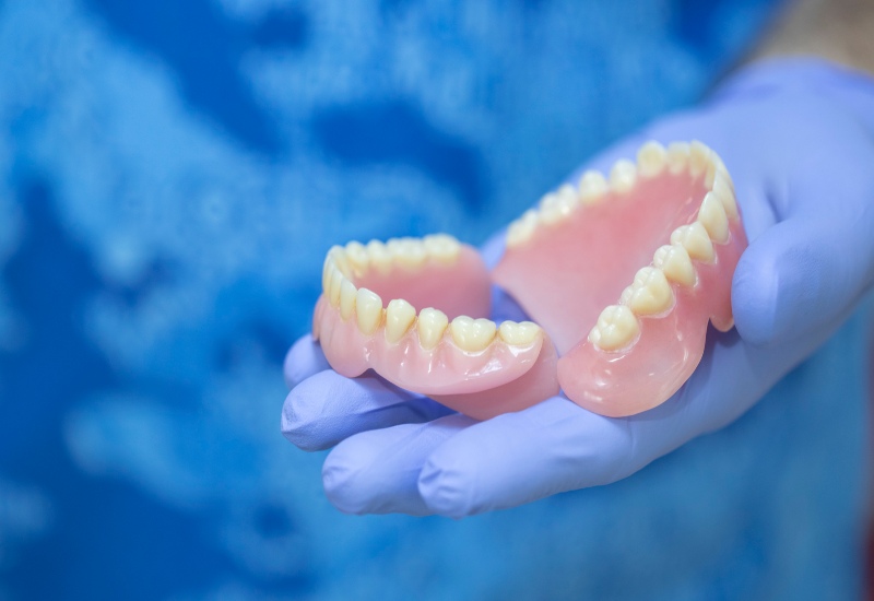 A gloved hand holding a full set of dentures in a clinic setting for Dentures in Monroeville, PA