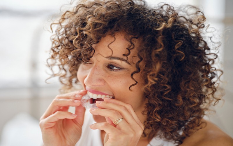A woman smiling while placing an Invisalign aligner, showcasing dental care in Monroeville, PA