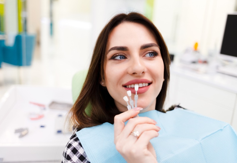 A woman comparing no-prep veneers in Monroeville, PA, with the tooth shade guide in a dental office