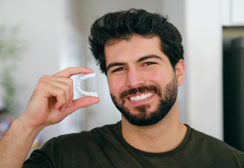 A smiling man holding an Invisalign clear aligner, showcasing teeth straightening in Monroeville, PA