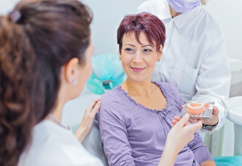 A patient viewing dentures as the dentist explains the implants vs. dentures options in Monroeville